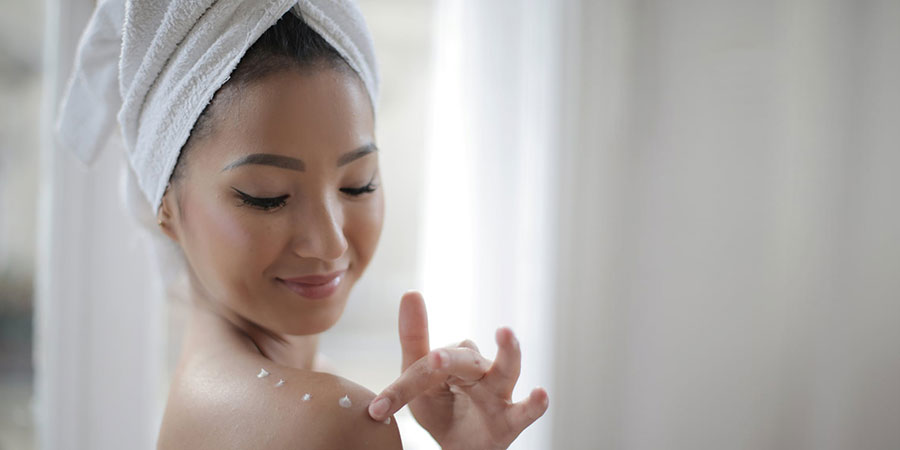 Asian woman with a white towel wrapped around her black hair touching her should with bits of lotion on it