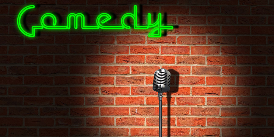 neon signage with the word comedy, metallic microphone and brick wall